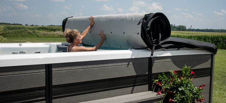woman rolling up the axis cover system while inside her swim spa